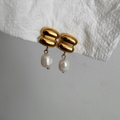 Gold earrings with pearl drops on a white fabric background